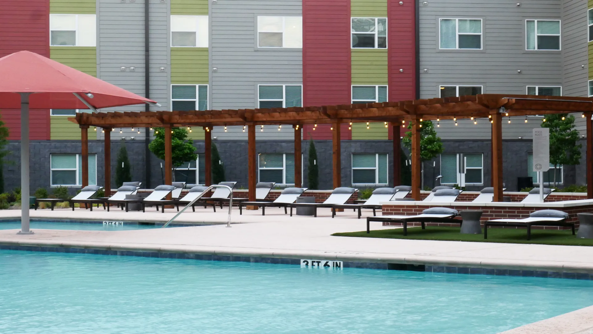 a pool with lounge chairs and umbrellas in front of apartment buildings at The Terra at University North Park